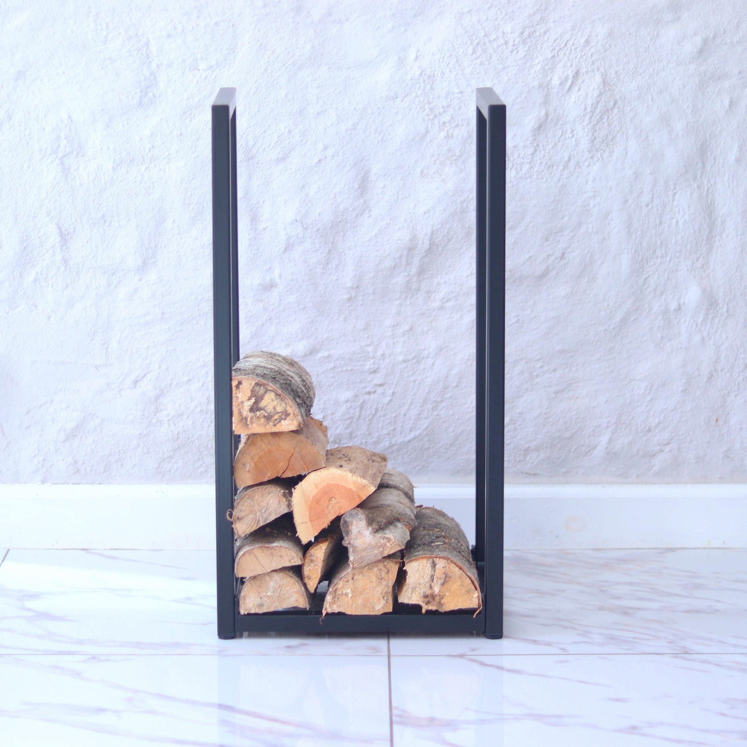 Black metal firewood holder with stacked logs against a white wall.