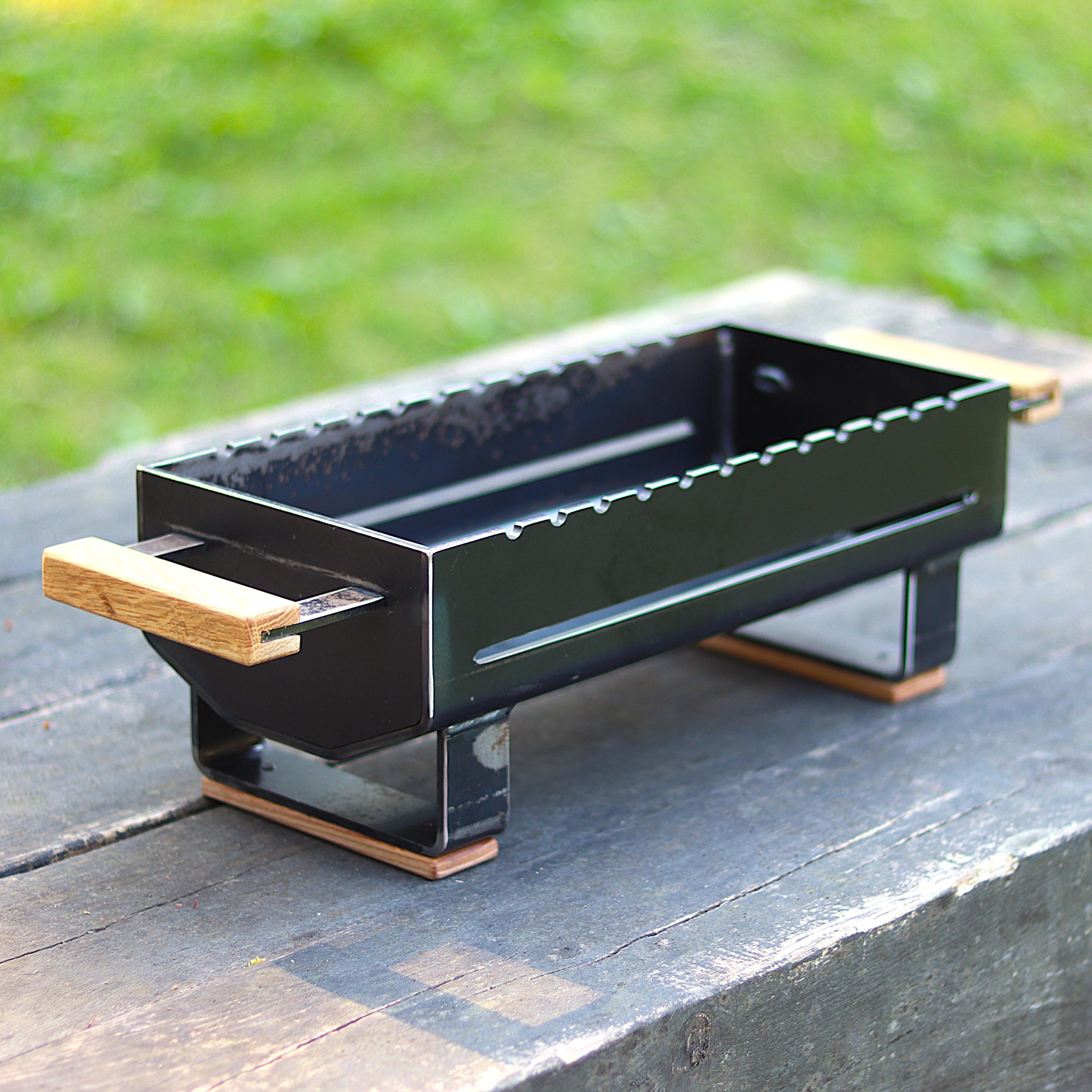 Black rectangular hibachi grill with wooden handles on a wooden surface with grass in the background