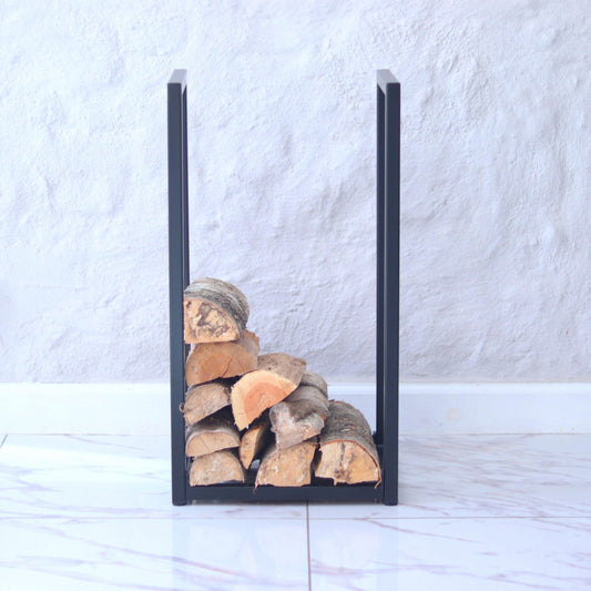 Black U-shaped metal firewood holder with stacked logs against a white wall